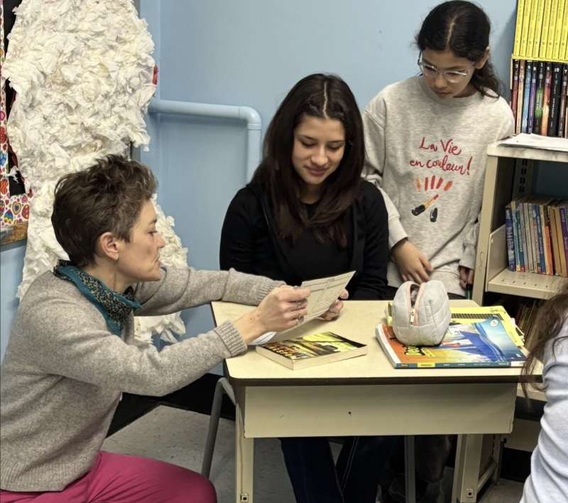 Photo of teaaching artist at a school deskw ith two students. Photo by Athanasia Papamichelakis